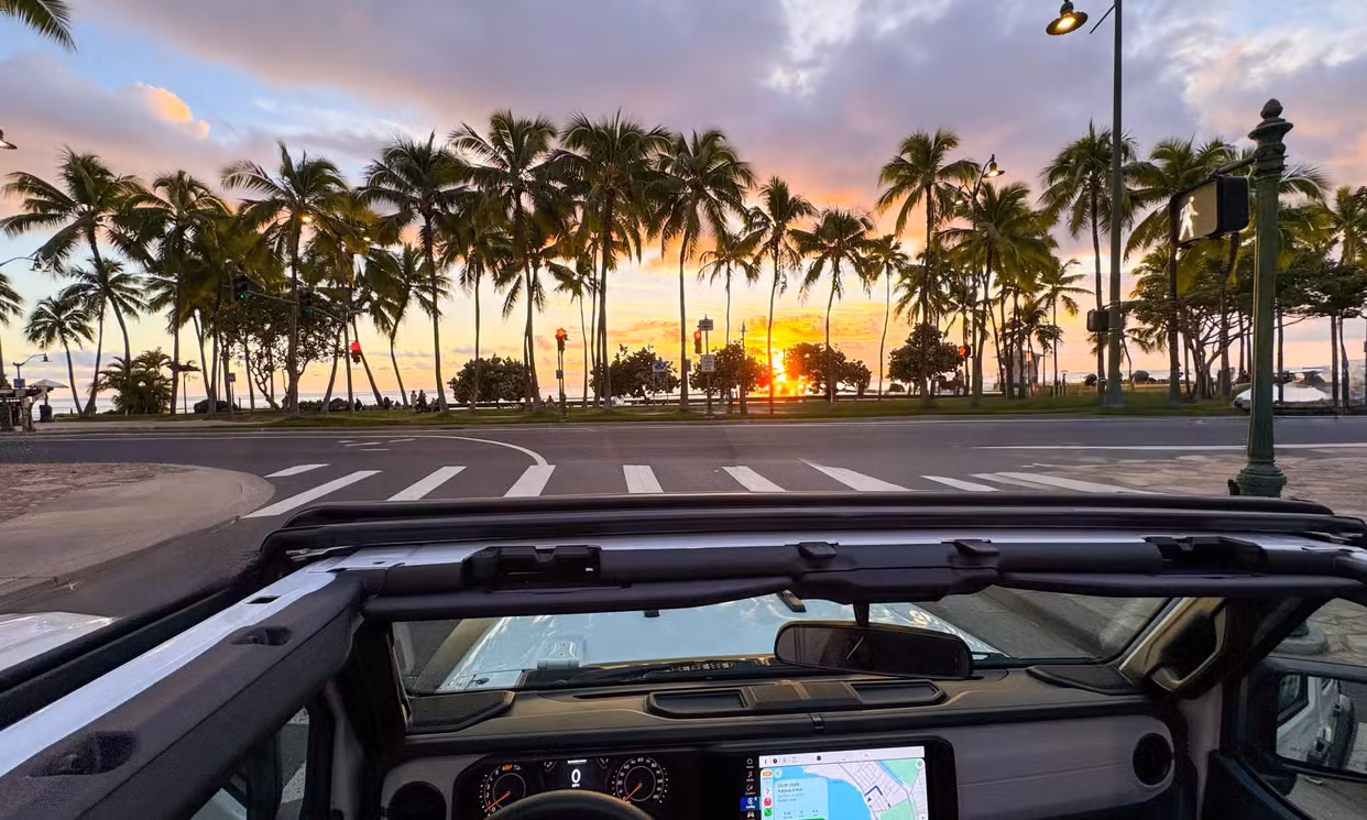 Blick aus einem offenen Jeep auf eine Straße auf Oahu bei Sonnenuntergang